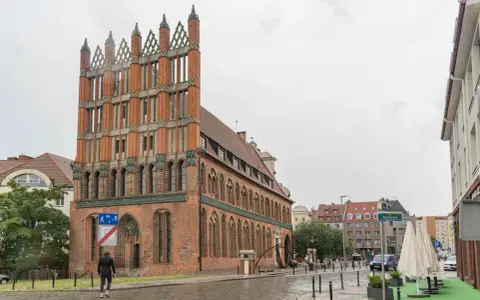 Ein Mann geht durch die regennasse **Stettin Altstadt** an einem Backsteingebäude mit Spitzdächern vorbei.