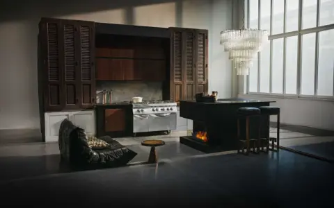 Ett kök med industriell känsla, inspirerat av Marie Olsson Nylander inredning. En stor gasspis, mörka träskåp och en modern köksö med eldstad.