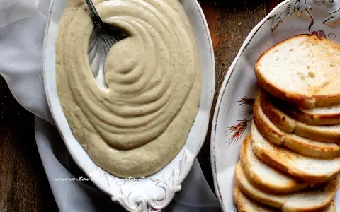 Salsa tonnata cremosa, con maionese, servita in un piatto ovale con fette di pane tostato.