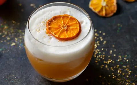 Ein cremiger Amaretto Cocktail mit einem getrockneten Orangenscheibchen und goldenem Glitzer.