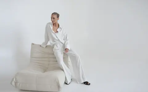 Elegancka kobieta w pasiastym komplecie, uosobienie quiet luxury, siedzi na kremowej sofie.