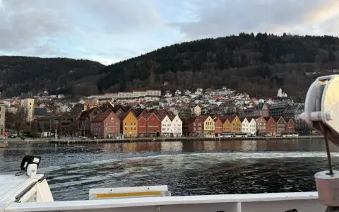 Bunte Holzhäuser am Kai von Bergen, mit einem bewaldeten Hügel im Hintergrund. Die bergen bahn ist hier nicht zu sehen, aber die Aussicht ist malerisch.