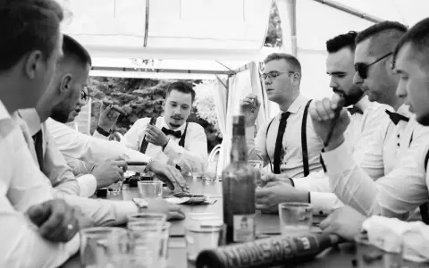 Panowie w eleganckich koszulach i szelkach świętują, paląc cygara i pijąc. Świetne kawalerski pomysły na wspólne chwile.