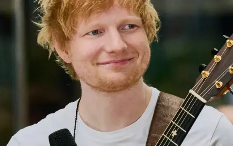 Ed Sheeran z gitarą, uśmiechnięty, w białej koszulce.
