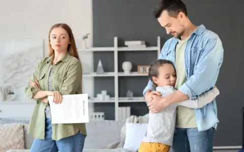 Ojciec tuli córkę, podczas gdy matka z dokumentem rozwodowym patrzy z boku. Przejęcie opieki nad dzieckiem przez ojca w trudnym momencie.