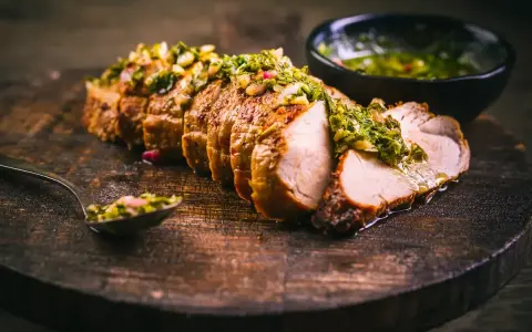 Jugoso solomillo de cerdo, cortado en rodajas y cubierto con una sabrosa salsa verde, servido en tabla de madera.