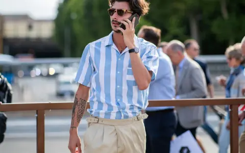Hombre con camisa a rayas azules y blancas y tiro pantalón alto color beige, hablando por teléfono.