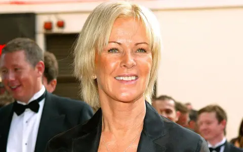 Anni-Frid Lyngstad, känd som Frida, ler med en hjärtformad halsband. Hon är klädd i en svart kavaj.