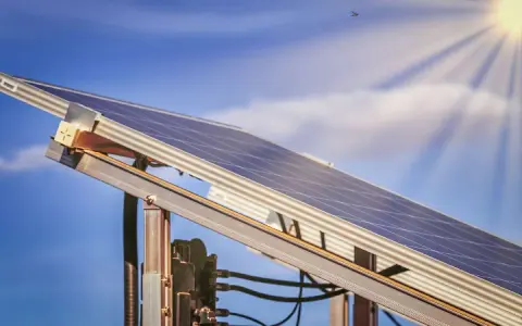 Ein Balkonkraftwerk MV fängt die Sonnenstrahlen ein. Der blaue Himmel mit Wolken und die Sonne im Hintergrund versprechen viel Energie.