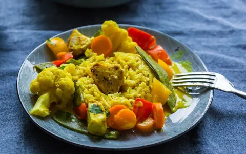 Ein Teller mit gelbem Reis, Blumenkohl, Karotten, Paprika und Erbsen. Ein köstliches Curry Geschnetzeltes, bereit zum Genießen.