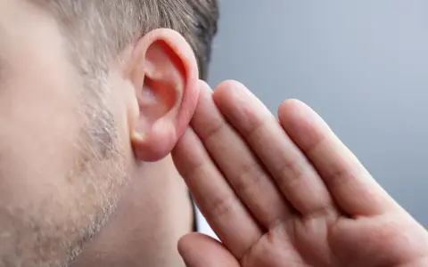 Mężczyzna przykłada dłoń do ucha, próbując usłyszeć coś mimo uczucia zatkanego ucha, być może z powodu zapalenia ucha.