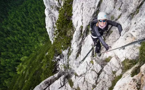 Kobieta wspina się po via ferrata w Dolomitach, z widokiem na gęsty las poniżej.