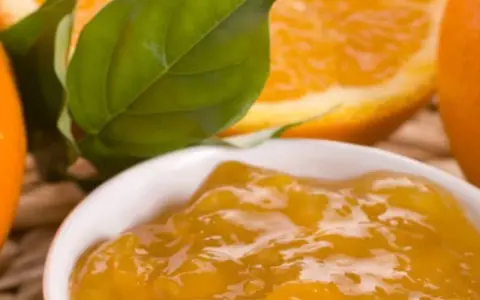 Una ciotola di marmellata di arance, con fette di arancia e foglie verdi sullo sfondo. Un'idea per un delizioso pesto al limone.