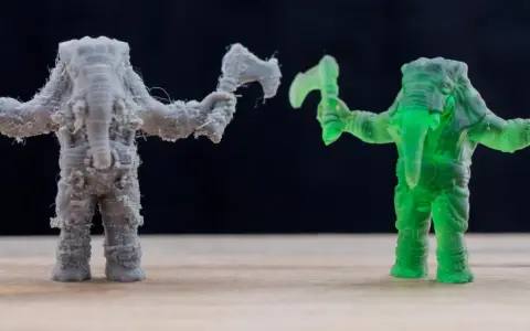 A grey FDM printed elephant warrior with stringing, and a translucent green resin printed elephant warrior, showcasing the difference between FDM vs resin printing.