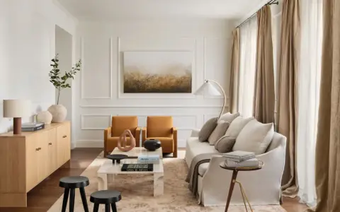 Elegante salón con salones con molduras en paredes, sofá blanco, sillones ocre y mesa de centro de mármol.