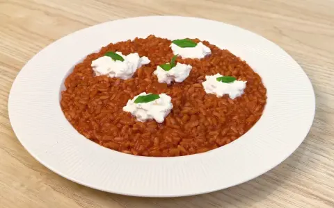 Un invitante risotto al pomodoro, arricchito da ciuffi di ricotta fresca e basilico, pronto per essere gustato.