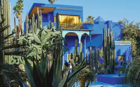 La **maison bleu Majorelle** se dresse fièrement, entourée d'une jungle de cactus et de palmiers. Un spectacle vibrant sous le ciel bleu.