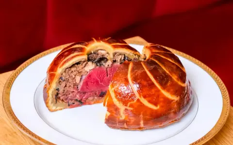 Un pâté en croûte aux couches généreuses, un délice d'antan origine, sur une assiette blanche bordée d'or.