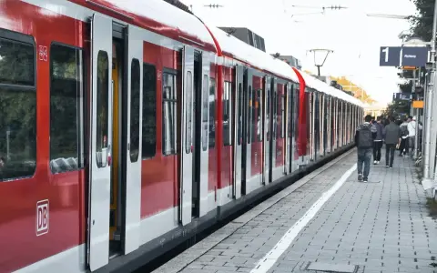 Czerwony pociąg na stacji. Ludzie czekają na peronie, zastanawiając się, jak zwrocic bilet.