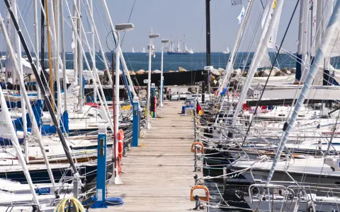 Viele Segelboote liegen im **Flensburg Hafen** an einem Holzsteg. Im Hintergrund segeln große Schiffe auf dem Meer.
