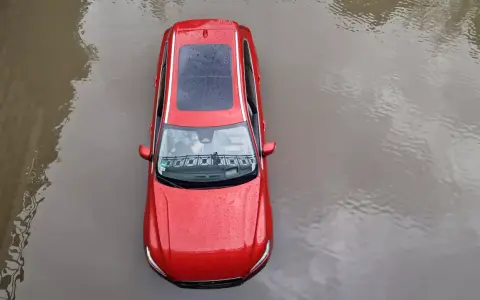 Czerwony samochód stoi w wodzie. Po powodzi czeka go osuszanie auta.