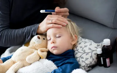 Bambino addormentato con febbre, la mamma controlla la temperatura. Vicino ci sono flaconi di antibiotico.