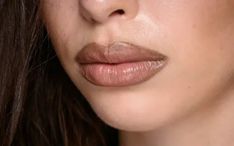 Labbra carnose e lucide, con un effetto naturale per ingrandire le labbra, evidenziate da un rossetto nude.