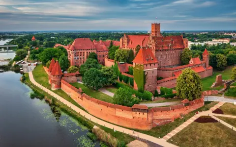 Malbork i okolice co zwiedzić? Potężny zamek krzyżacki nad rzeką, otoczony murami i zielenią, zaprasza do odkrywania historii.