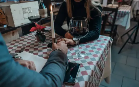 Romantyczna kolacja, świeca, wino i dłonie splecione na stole. Widać, jak angażuje się mężczyzna, skupiony na partnerce.