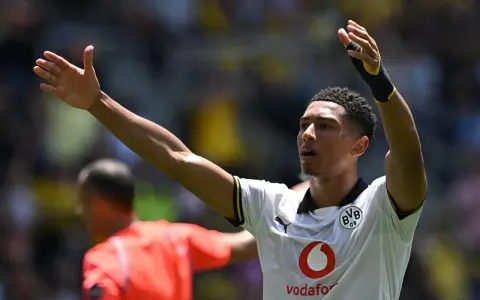 Jude Bellingham, con los brazos en alto, celebra un gol. El joven jugador del Dortmund, con su camiseta blanca, inspira a la afición.