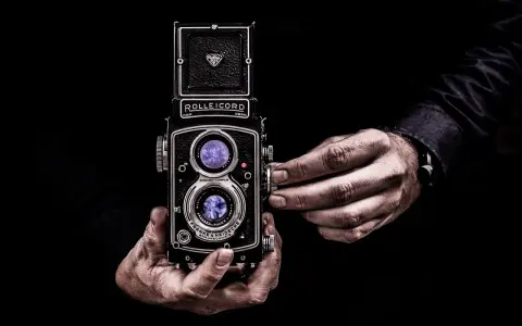 Dwie ręce trzymają aparat Rolleiflex, jedna reguluje ostrość. Sztuka fotografii, zasada złotego środka w kadrze.