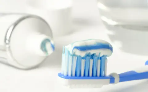 Szczoteczka z biało-niebieską pastą do zębów, zawierającą **sodium fluoride**, gotowa do porannej higieny.