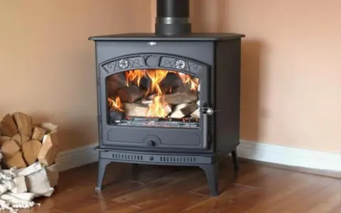 Poêle à bois en fonte, allumé, avec une pile de bois à côté. Un bon entretien assure une longue durée de vie à ce poêle à bois.