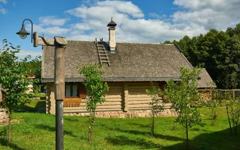Drewniany dom z kamienną podmurówką i gontowym dachem, otoczony zielenią. To malownicze grunty rolne zabudowane, gdzie tradycja spotyka się z naturą.