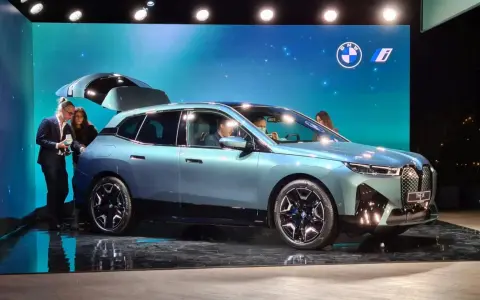 Jasnoniebieski elektryczny SUV BMW iX z otwartą klapą bagażnika na scenie.