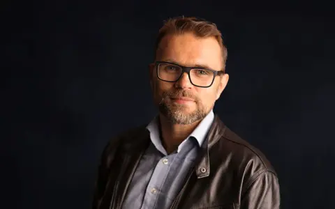Jacek Bartosiak, autor książek, w okularach i skórzanej kurtce, patrzy w obiektyw.
