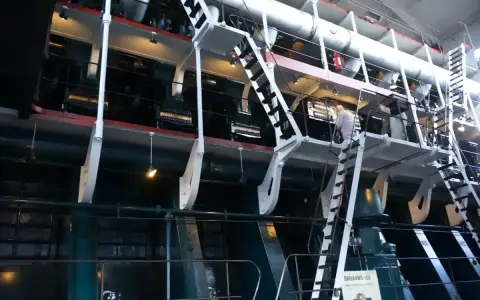 Ogromna, wielocylindrowa jednostka napędowa, prawdopodobnie największy silnik na świecie, z metalowymi schodami i platformami dla obsługi.