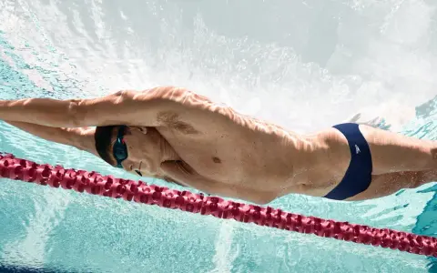 Un nageur en plein effort, profitant des bienfaits natation. La lumière joue sur son corps musclé, soulignant la puissance de ses mouvements sous l'eau.