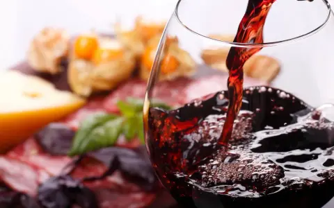 Rotwein wird in ein Glas gegossen, daneben Käse und Wurst. Welcher Wein hat am wenigsten Kalorien?