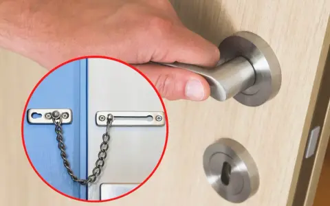 Dłoń otwiera drzwi, w kółku widoczna jest łańcuszkowa blokada drzwi.