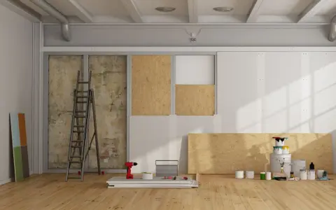 Chantier de rénovation avec panneaux de bois, échelle, outils et pots de peinture.
