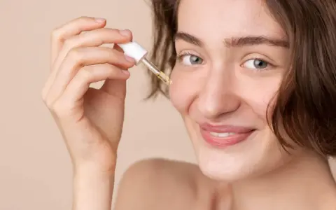 Une femme souriante applique une goutte de sérum à la vitamine C sur son visage. C'est le moment idéal pour utiliser la vitamine C sur le visage pour une peau éclatante.