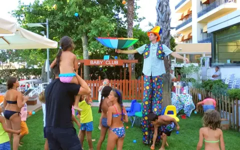 Hotel con biberoneria: animazione al Baby Club con un clown che intrattiene i bambini con palline colorate e un ombrello arcobaleno.