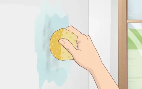 Mano limpiando una mancha en una pared blanca con una esponja. Aprende como limpiar paredes blancas fácilmente.
