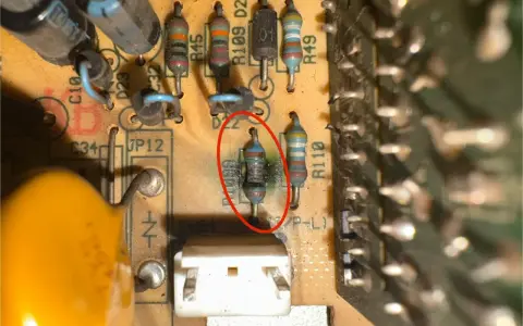 Uszkodzony opornik z czerwonym okręgiem na płytce drukowanej, obok innych elementów elektronicznych.