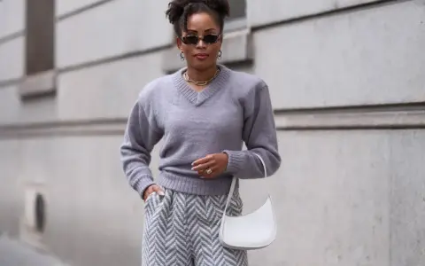 Eine Frau in grauem Pullover und Hose mit Zickzackmuster. Sie trägt eine weiße Tasche. Ein Beispiel, welche Farben passen zu grau.