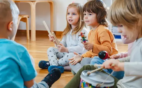 Kinder musizieren mit Holzstäben, Rasseln, einer Trommel und einem Maracas. Welche Instrumente gibt es?