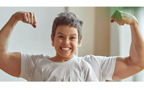 Chłopiec z miną jak po **buncie 5 latka** pokazuje swoje małe bicepsy, podczas gdy za nim widać potężne ramiona taty.