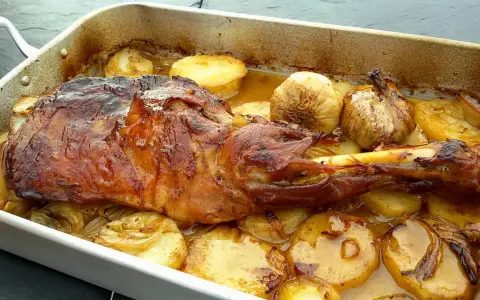 Delicioso cordero asado en una bandeja con patatas doradas y ajos enteros. Un festín para los sentidos.