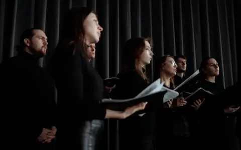 Chór w czarnych strojach, z nutami w rękach. Słychać głosy męskie i kobiece, tworzące harmonijną całość.